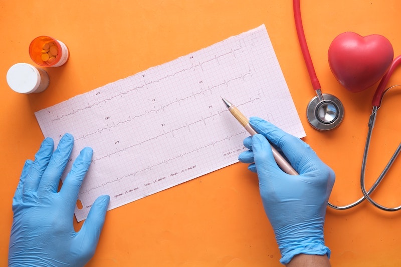 Ein Arzt sieht sich die Herzfrequenz eines Patienten an, neben ihm sind ein Stethoskop, Herzmodell und Tabletten zu sehen