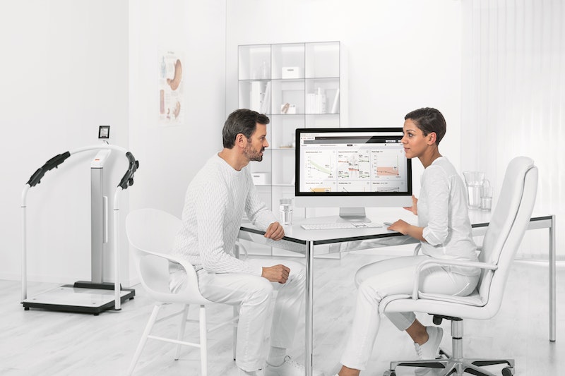 Ein Arzt und eine Ärztin sitzen in einer weißen Arztpraxis vor dem Computer und sehen sich Gesundheitswerte an